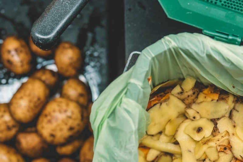 Photo of a sink with potatoes and potato peel in a compostable bin liner in a kitchen caddy. 