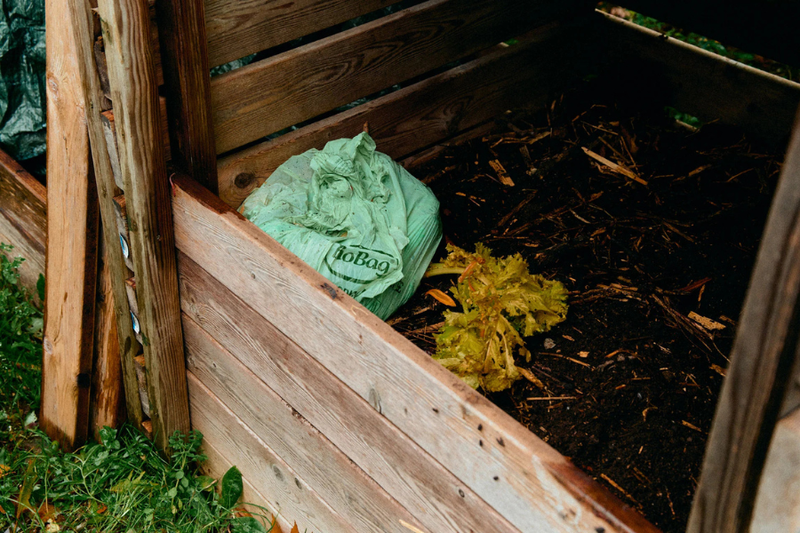 Photo of a full compostable bin bag in a compost heap with soil and organic waste. 