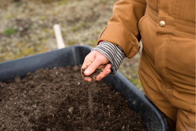 Person holding soil over a bin of compost