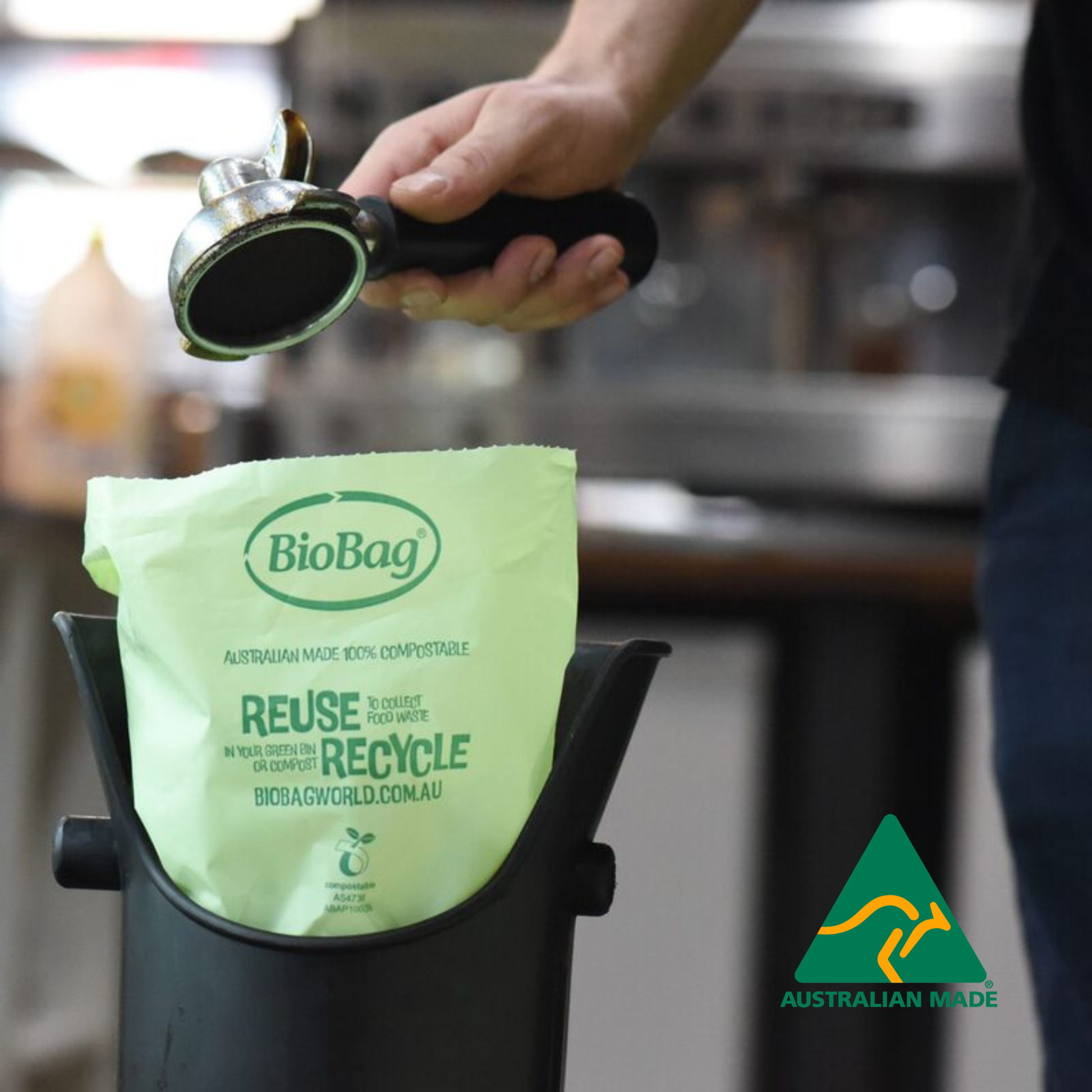 Person using a coffee machine coffee grip over a coffee knock with a BioBag compostable bag with 'Reuse Recycle' text in a cafe setting.
