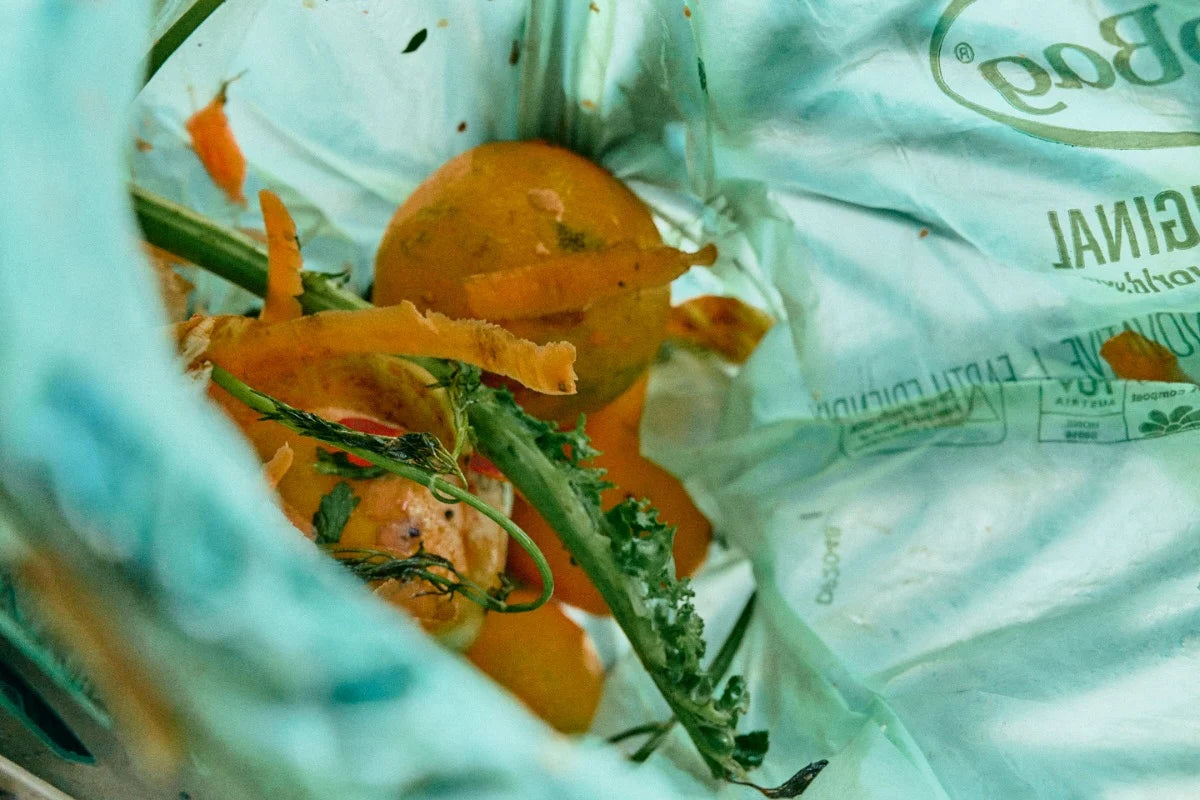 Compostable BioBag bin bag with food waste including carrots and greens, with a brand name visible.