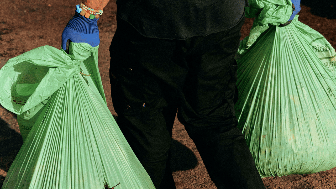 Person holding two BioBag green compostable bin liners with gloves on a dirt ground