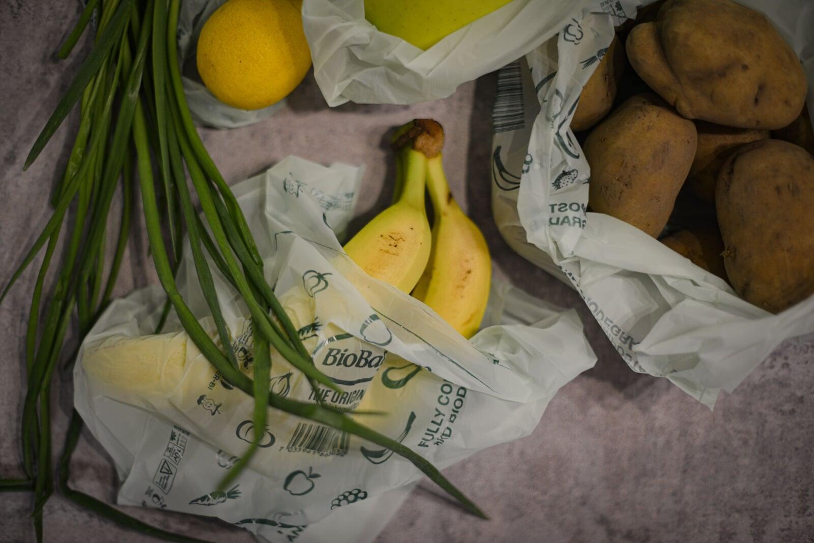 BioBag compostable produce bags being used with produce including bananas, lemons, and potatoes on a textured surface.
