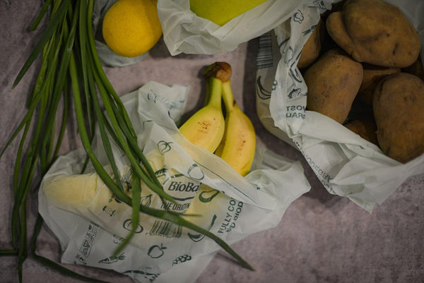 BioBag compostable produce bags being used with produce including bananas, lemons, and potatoes on a textured surface.