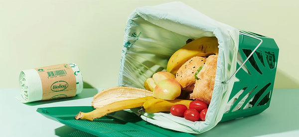Compostable caddy bin liner filled with fruits and vegetables next to a roll of BioBag caddy bin liners. 