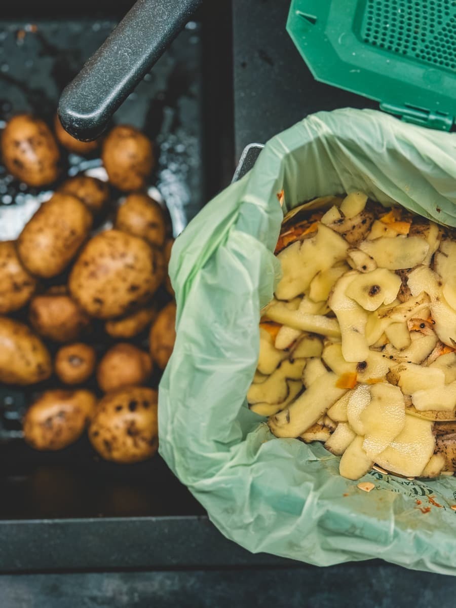 Photo of a kitchen waste caddy being used at a kitchen sink with potatoes and the peels in the BioBag compostable caddy liner